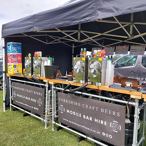 Long mobile bar under a large marquee serving cold craft beer to guests